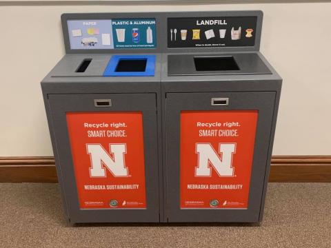 The new UNL recylcing and landfill stations are gray and have red graphics on them with the university branding and info about what people can recylce